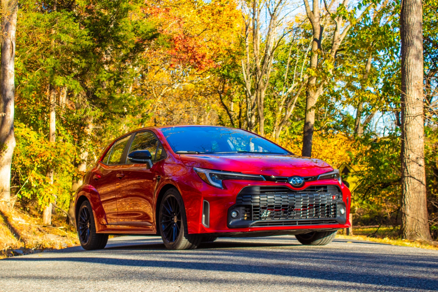 A 2023 Toyota GR Corolla in Supersonic Red with fall foliage in the background.