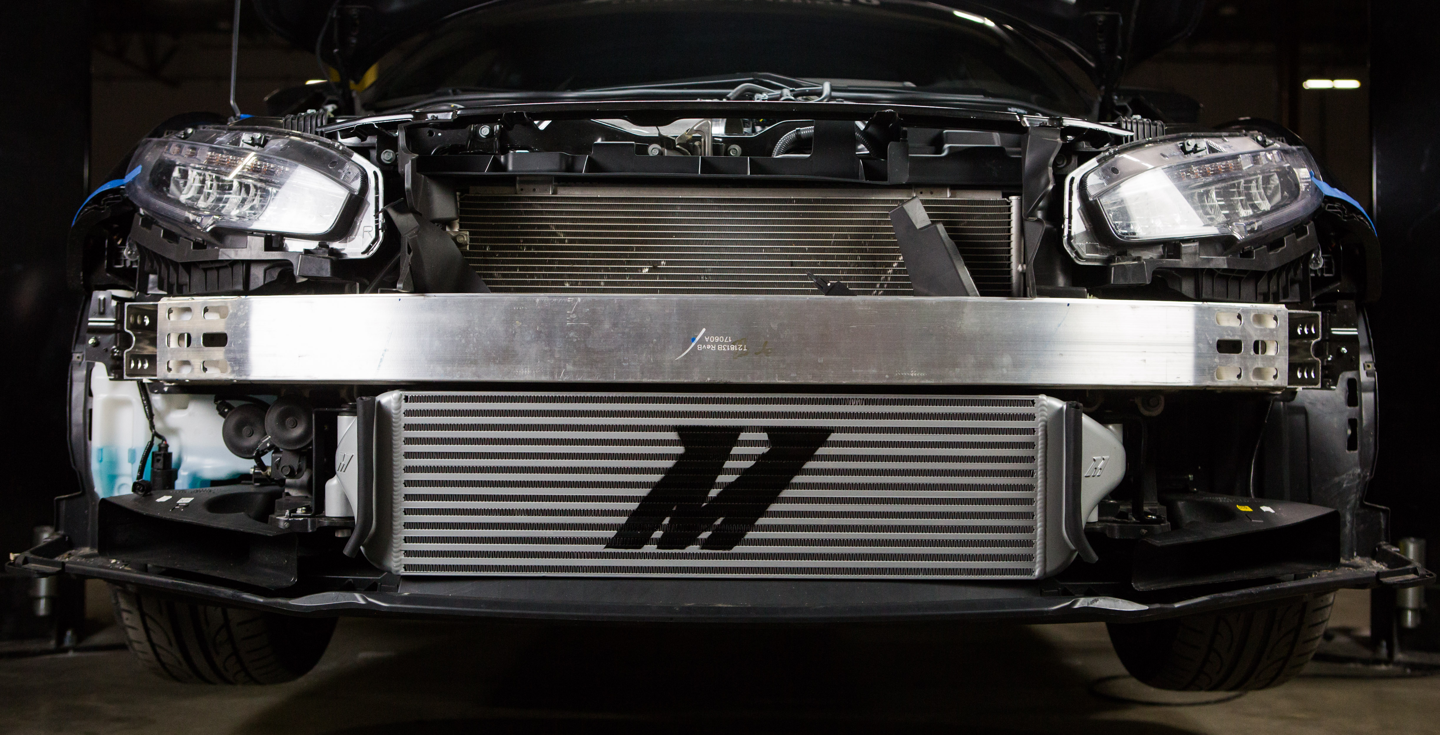 An image of a performance Mishimoto intercooler installed on the front of a car with its bumper removed.