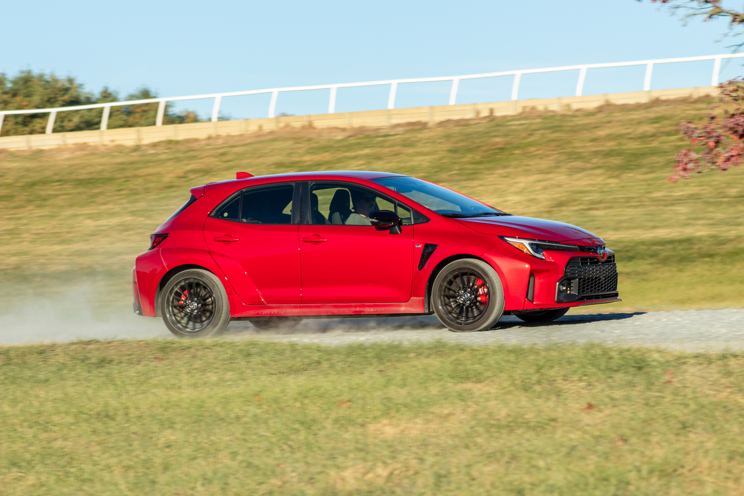 A Toyota GR Corolla in Supersonic Red driving quickly down a dirt road.